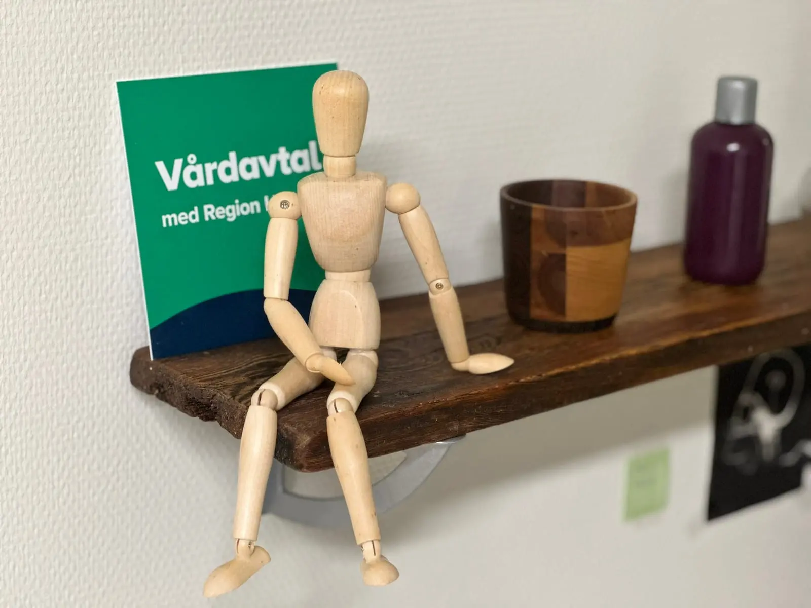 Träfigur som sitter på en hylla intill skylten Vårdavtal med Region Halland